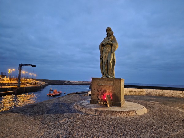 Harbour statue looking out to sea with the port and a small boat nearby in Puerto de la Cruz.
