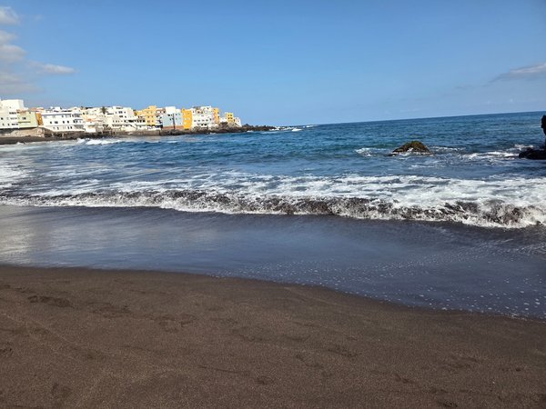 Gentle wave rolls onto the volcanic black sand in front of Punta Brava's seafront houses.