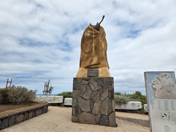 Monument on a stone plinth with an information board at a Punta del Hidalgo viewpoint.
