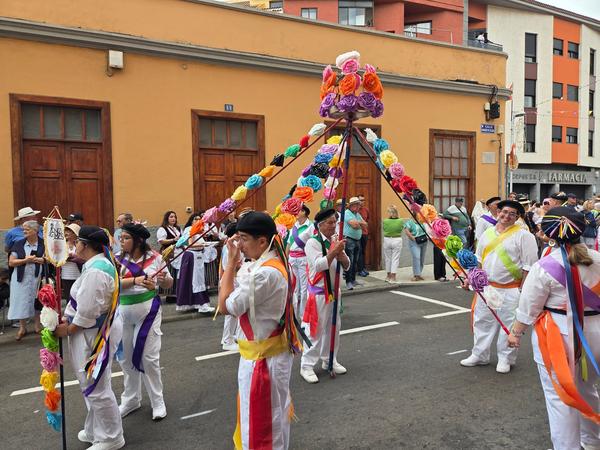 Dance troupe carrying a colorful pole adorned with artificial flowers.
