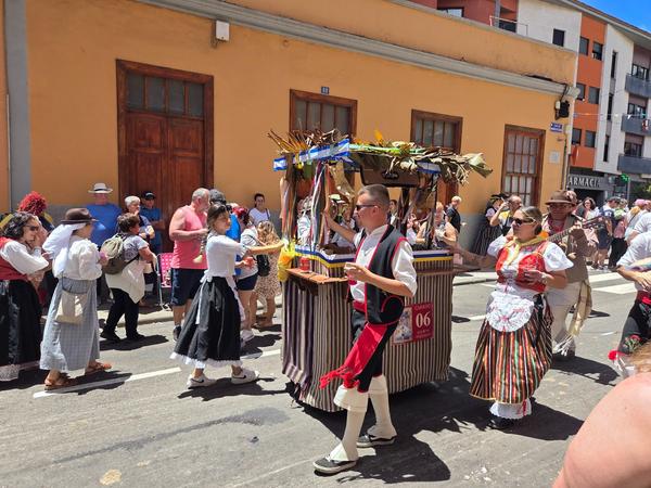 Colorful folk group dancing and moving with a small decorative cart.