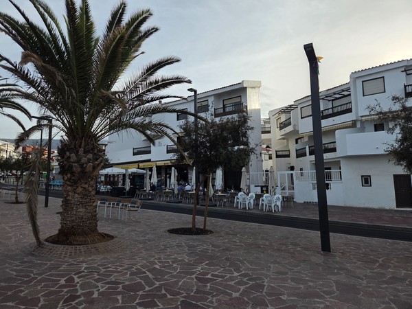 Row of terrace cafés on the Playa San Juan promenade with umbrellas and outdoor seating.