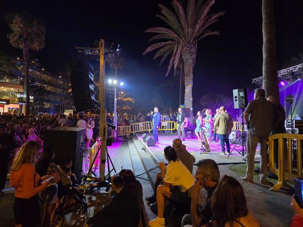 A lively open-air concert during the San Juan Festival with crowds enjoying the performance near palm trees.