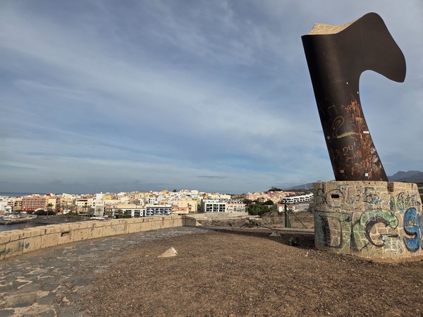 Abstract metal sculpture on the headland above Playa San Juan with town skyline behind.