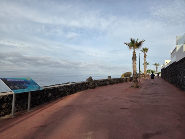Promenade curve at Playa San Juan with benches casting long morning shadows beside the rocky shoreline.