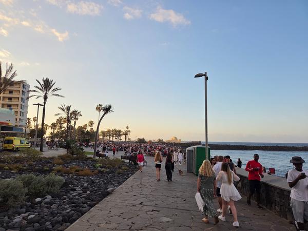 People arriving along the seaside promenade during sunset, heading to the San Juan Festival in Puerto de la Cruz.