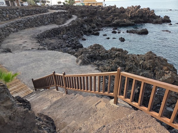 Wooden stairway descending through lava rock terraces to the shoreline at Playa San Juan.