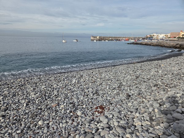 Rounded grey pebbles on the beach near Playa San Juan with the harbor in the distance.