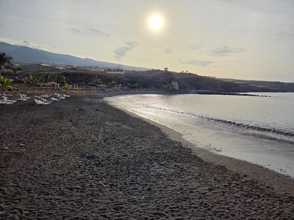 Early-morning view across Playa San Juan with glistening shoreline and gentle waves under a rising sun.
