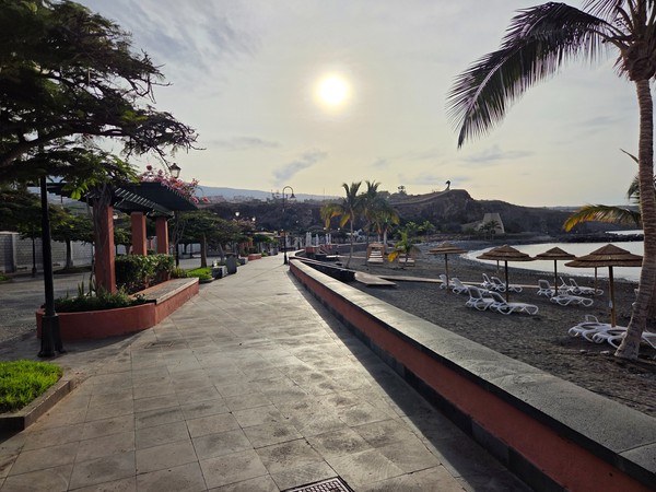 Curving seafront promenade at Playa San Juan with wooden decking, railing, palms and outdoor terraces facing the ocean.