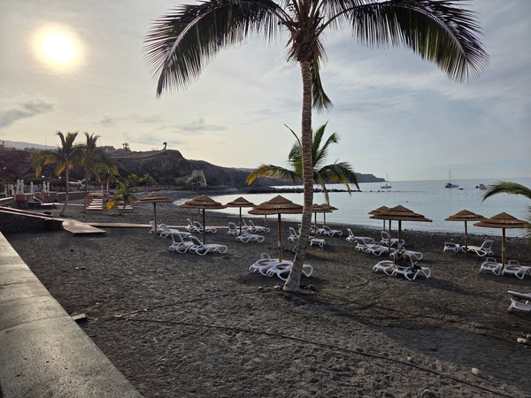 Curving shoreline of Playa San Juan with pebbles in the foreground and the town and beach facilities across the bay.
