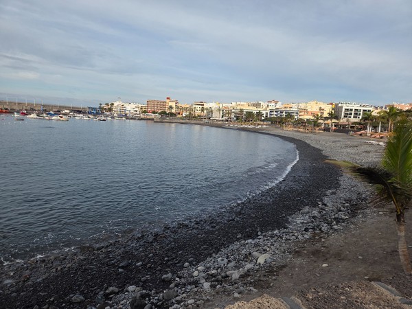 Wide view of Playa San Juan’s curved black-sand bay with calm water and breakwaters in the distance.