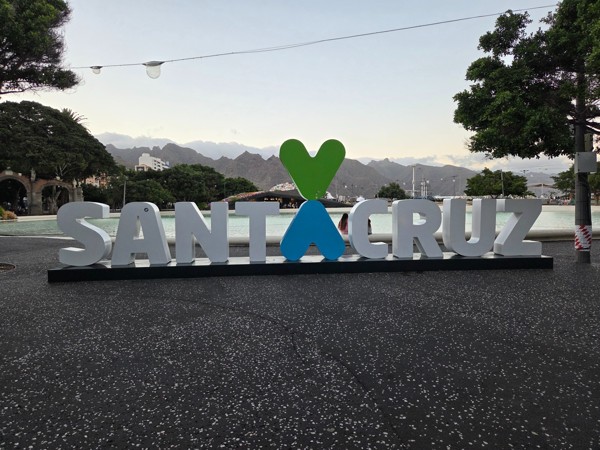 Large SANTA CRUZ sign with heart motif by the lagoon near Plaza de España, mountains in the background.