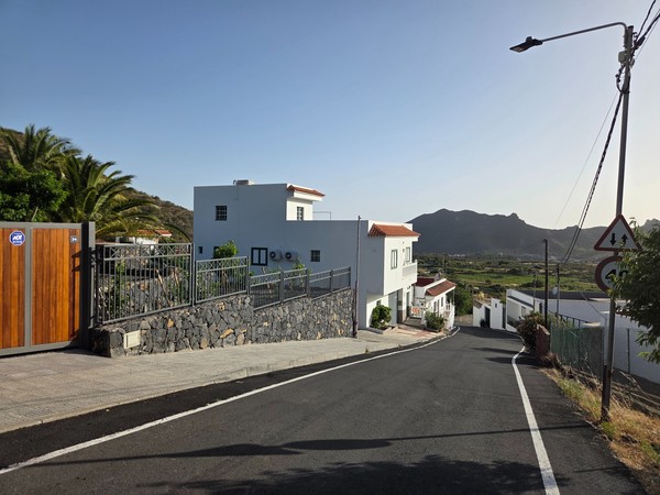 Whitewashed homes line a steep street in the municipality of Santiago del Teide with a jagged ridge in the distance.