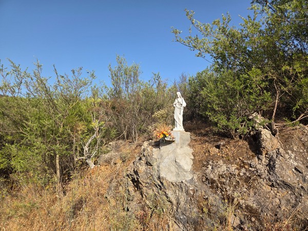 A small Marian statue shrine with flowers set among the scrubland and rocks above Santiago del Teide.