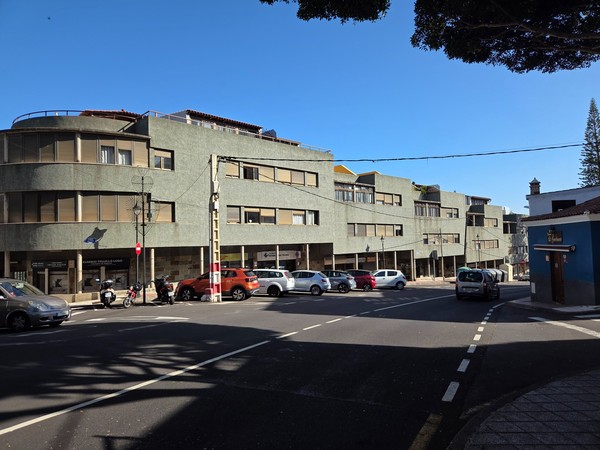 Curved, modernist-style building on a Tejina street with shops and parked cars.