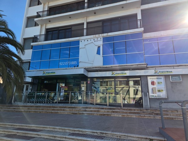 Entrance to the SuperDino supermarket in Tejina beneath a modern glass-fronted building.