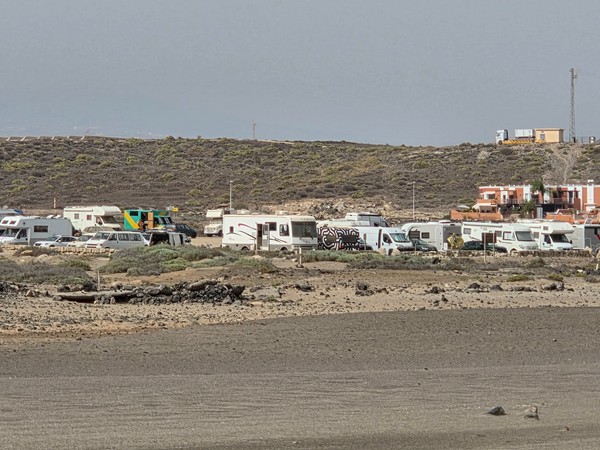 Line of camper vans and motorhomes parked near La Tejita’s backshore, showing the beach’s popularity with van travelers.