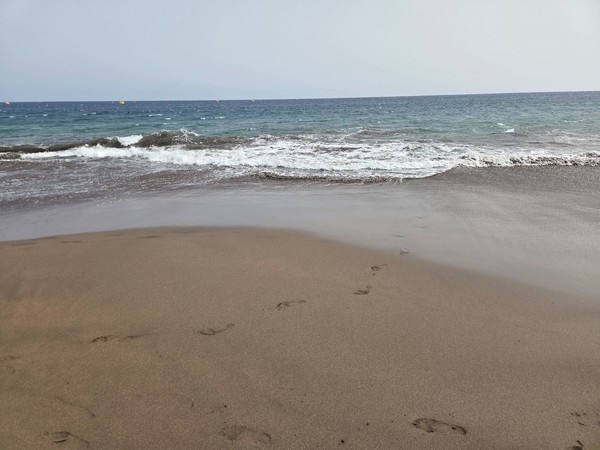 Small Atlantic waves folding over La Tejita’s dark sand with footprints fading as the water recedes.
