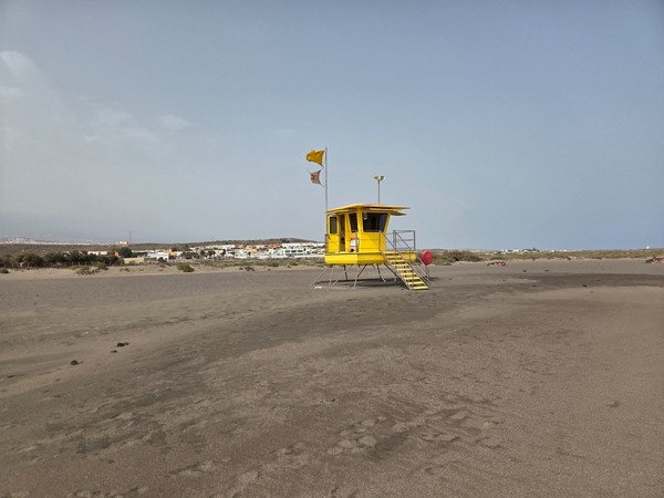 Prominent yellow lifeguard hut at La Tejita standing on stilts above the sand with safety flags flying.