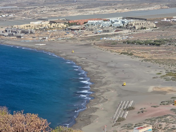 La Tejita Beach looking toward the red volcanic cone of Montaña Roja under a clear sky and calm Atlantic.