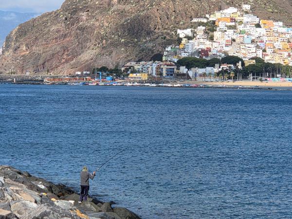 A local fisherman tries his luck along the rocky breakwater, framed by the colorful village of San Andrés in the background.