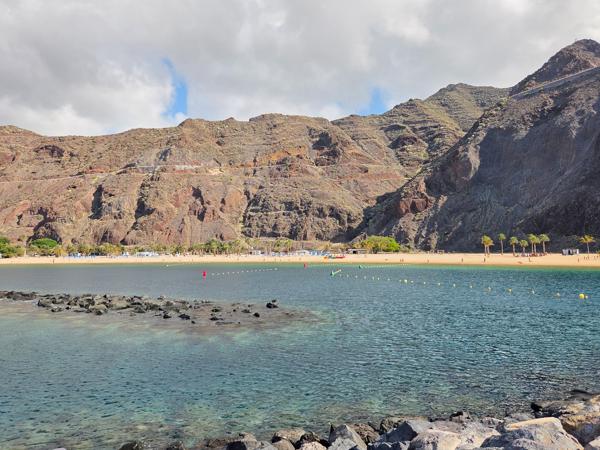 This view captures the northern tip of the beach where the lush cliffs meet the fine sand and crystal waters.