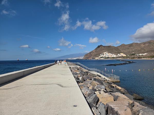A sweeping panoramic shot from above shows the protective breakwaters and full stretch of Playa de Las Teresitas.