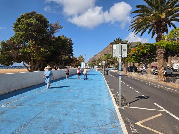 The blue-painted pedestrian lane runs parallel to the beach, encouraging walking or jogging with ocean views.