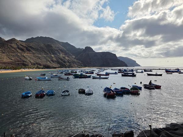 A dramatic view of anchored boats under an overcast sky captures the contrast between sunny shores and moody skies.