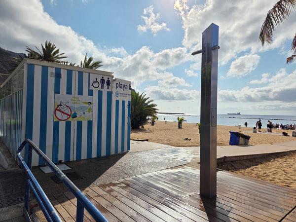 Beach facilities include showers and accessible restrooms, kept clean and visible with striped blue-and-white cabins.