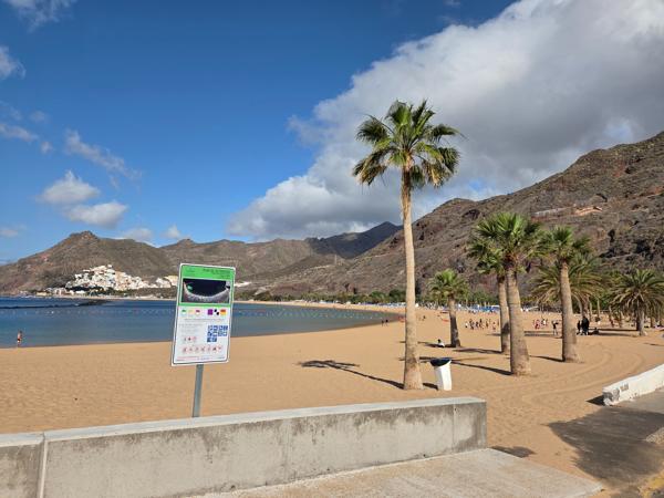 An official Playa de Las Teresitas sign stands at the center of the promenade, listing rules, services, and safety tips.